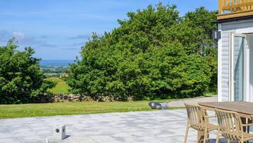 A pool with a stone deck, a wooden table with chairs, and a view of a green landscape and ocean.