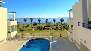 A pool area with a view of the sea, surrounded by palm trees and a well-maintained lawn.