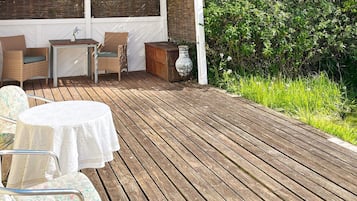 Una terraza de madera con mobiliario exterior, incluyendo una mesa y sillas, y un jarrón decorativo.