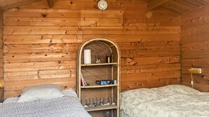 Acogedora habitación tipo cabaña con dos camas, una pared de madera y una estantería con libros y velas.