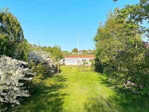 A pathway leading to a building with a red roof, surrounded by lush greenery and flowering shrubs. - 6 Person Holiday Home in Knebel (Knebel)