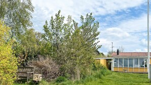 Un espacio cubierto de césped con un banco, un edificio con amplios ventanales y un árbol.