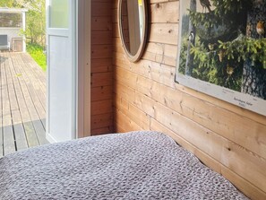 Una habitación con pared de madera, un espejo redondo y un cuadro con pájaros.