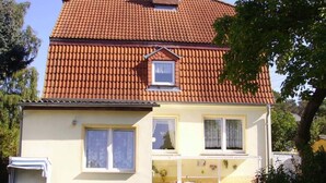 A two-story house with a red-tiled roof, a small attic window, and a front porch with a chair and a small table. - to the Beach Modern Retreat (Lubmin)