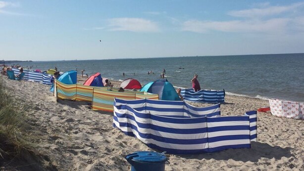A beach with striped beach umbrellas and tents, sandy beach, and the ocean. - to the Beach Modern Retreat (Lubmin)