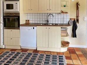 A compact kitchen with a built-in oven, microwave, and dishwasher, a sink with a faucet, and a tiled backsplash. - 5 Star Holiday Home in Odeshog (Odeshog)