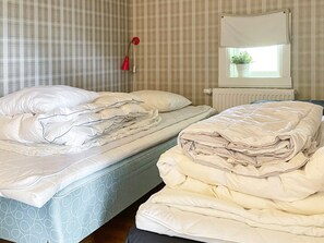 A room with two beds, one with a patterned mattress and the other with a plain one. There is a window with a plant on the sill and a red object hanging on the wall. - 5 Star Holiday Home in Odeshog (Odeshog)
