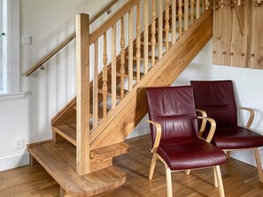 A wooden staircase with a handrail, wooden steps, and a landing area with two leather chairs.