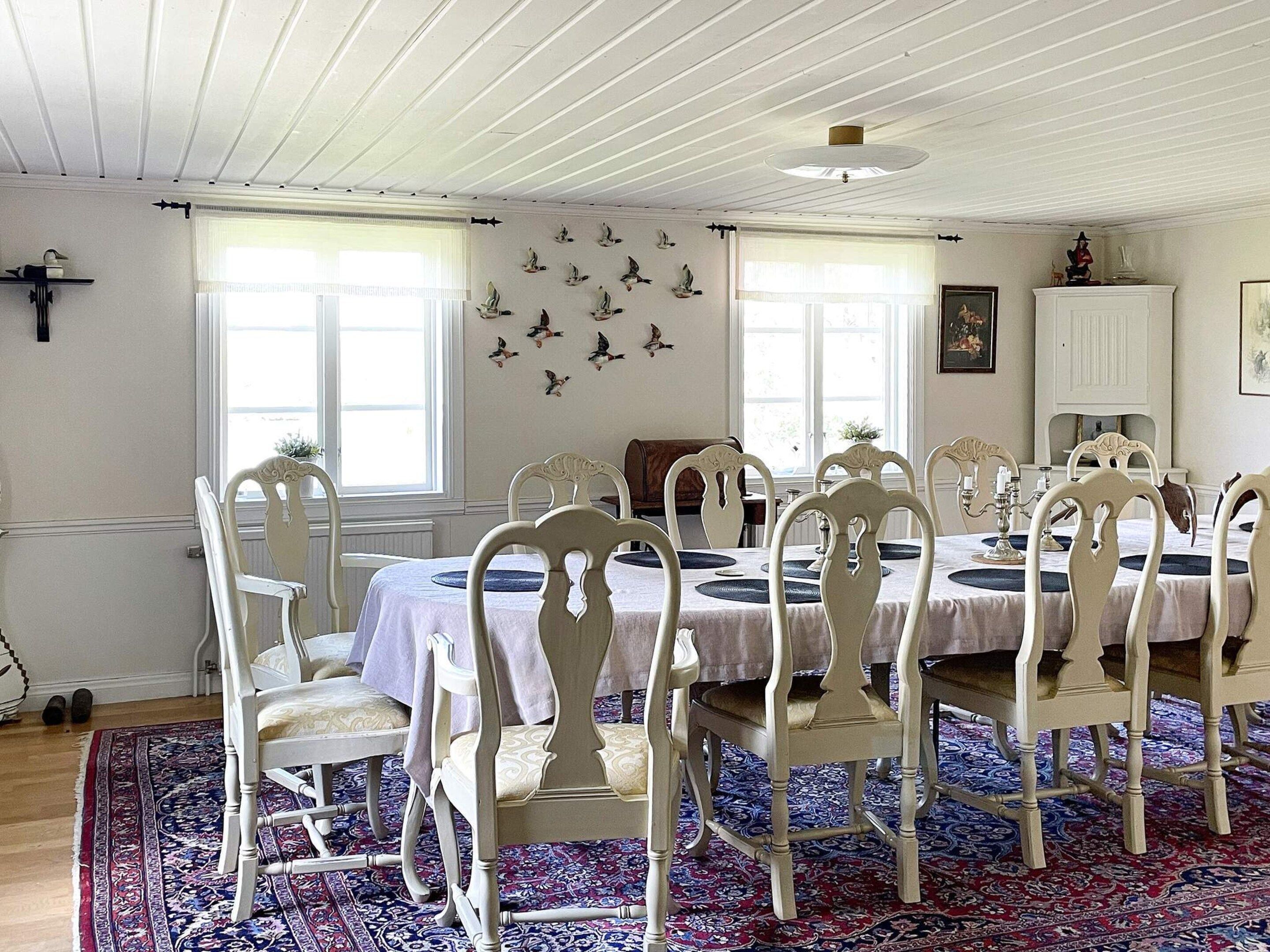 A dining area with white chairs and a table, a patterned rug, and a wall with bird decorations.