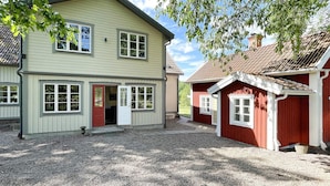 A two-story building with a gravel driveway, a red door, and a small attached structure with a red roof.