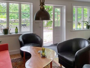 Une pièce avec une grande fenêtre, un fauteuil en cuir noir, une table basse en bois et un canapé rouge.