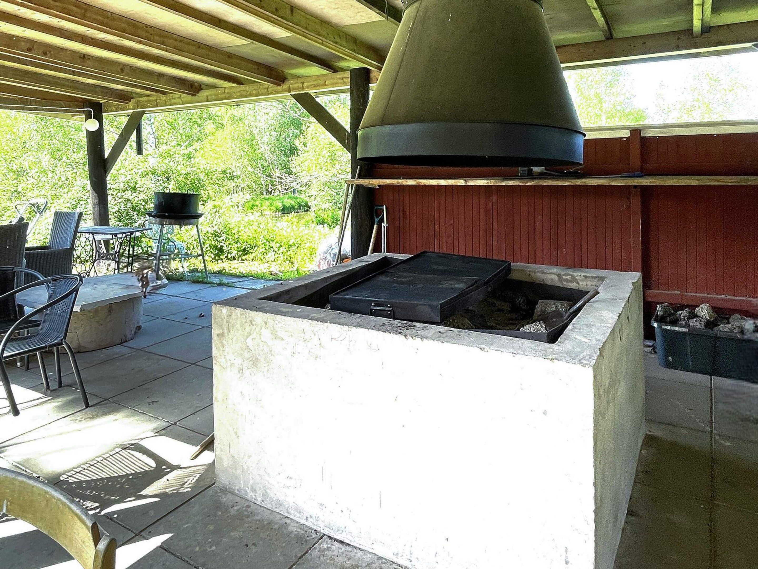 An outdoor patio with a grill station, seating area, and a view of greenery.