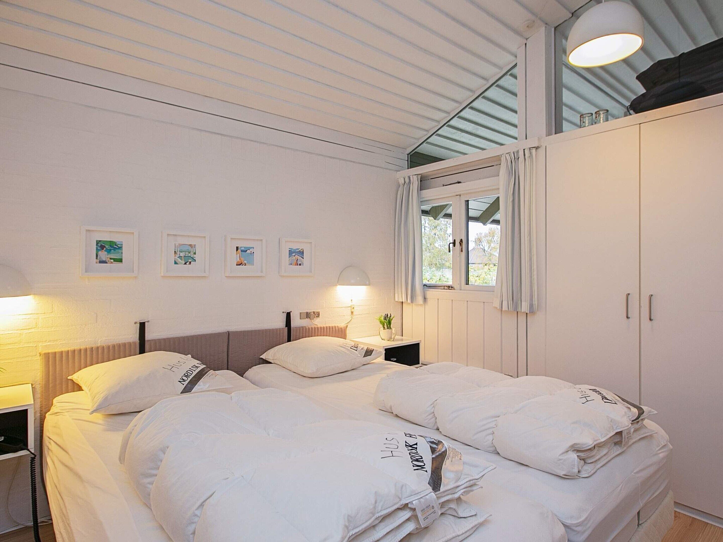 A bedroom with a bed, bedside tables, a window with curtains, and wall-mounted artwork.