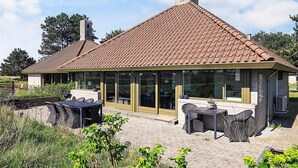 A house with a tiled roof, a chimney, and a covered patio area with outdoor furniture. - 5 Person Holiday Park Home in Karrebaeksminde (Karrebæksminde)