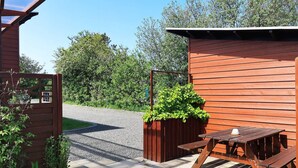 Un espace extérieur aménagé avec des sièges en bois, comprenant une table et des bancs, entouré d’un chemin de gravier et de verdure.