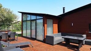 A modern outdoor deck with a wooden floor, a glass door leading to a covered patio, and outdoor furniture. - 6 Person Holiday Home in Vestervig (Vestervig)
