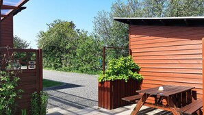 A wooden outdoor seating area with a table and benches, a wooden fence, and a gravel path. - 6 Person Holiday Home in Vestervig (Vestervig)