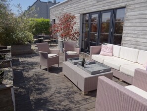An outdoor patio with wicker furniture, a white sofa, and a serving tray with glasses and a bottle. - Bright Attic With Sea Breeze (Nieuwpoort)