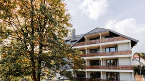 Ein modernes, zweistöckiges Haus mit Balkon, Auffahrt und einem großen Baum im Vordergrund.