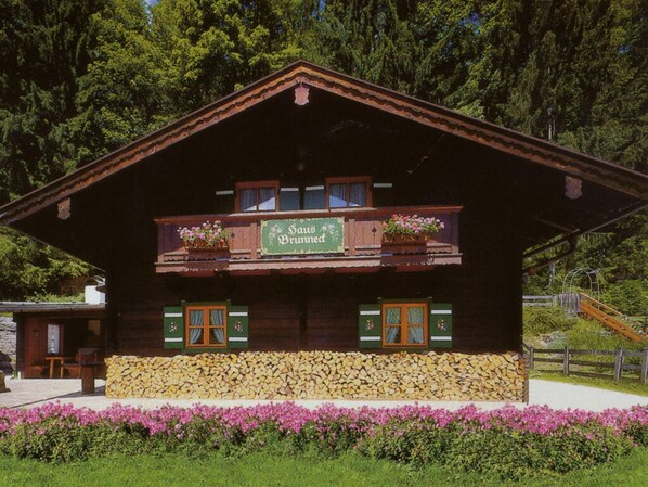 A traditional wooden chalet with a balcony, a sign reading "Gasthof Brummsee," and a stone foundation.