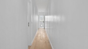 A narrow, white-walled hallway with wooden flooring leading to a door at the end. - Renovated Apartment for Family (Blankenberge)