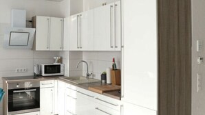 A modern kitchen with white cabinets, a microwave, an oven, and a wooden countertop. - Kickelhahn Comfortable Holiday Residence (Geratal)