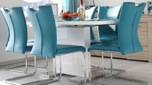 A modern dining area with a white table, teal chairs, and a large flat-screen TV mounted on the wall. - Kickelhahn Comfortable Holiday Residence (Geratal)