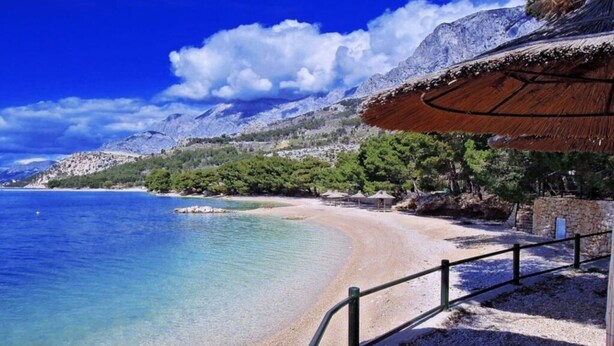 A beach with clear blue water, a sandy shore, and a mountainous backdrop. - Holiday Apartment Beach House Iva App. 3 (Gradac)