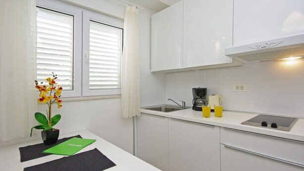 A compact kitchen with white cabinets, a sink, a coffee maker, and a small table with a plant and papers. - Holiday Apartment Beach House Iva App. 3 (Gradac)
