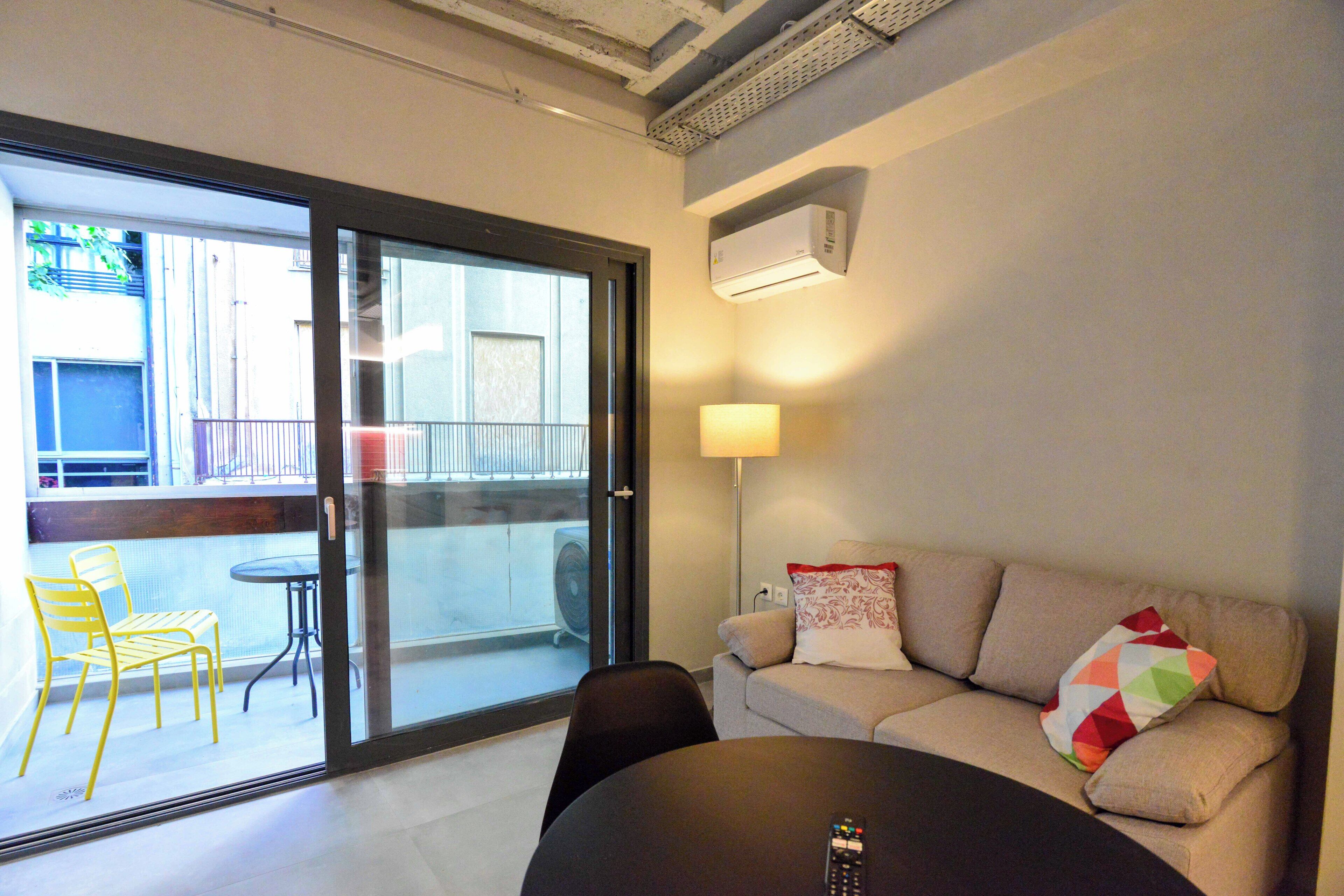 Un salon moderne avec un canapé, une table et une porte vitrée donnant sur un espace extérieur aménagé avec des chaises.