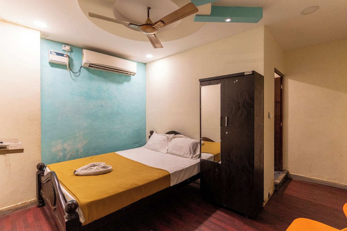 A single bed with a yellow bedspread, a ceiling fan, an air conditioning unit, and a wardrobe.