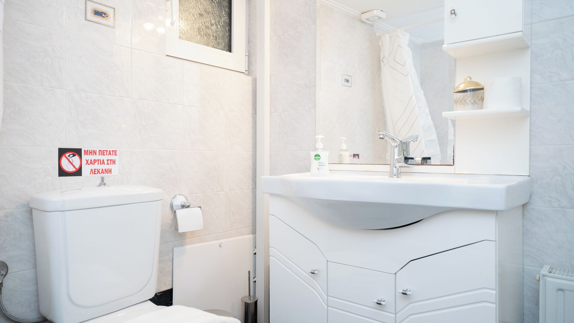 Une salle de bain moderne avec des toilettes, un lavabo et un miroir. Un panneau indiquant qu'il est interdit de fumer est visible sur le mur.