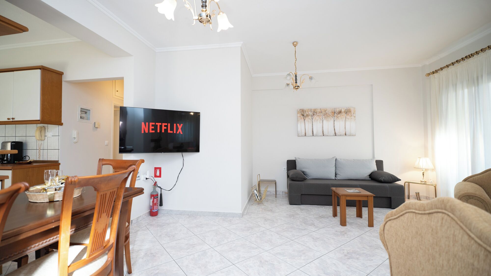 Een moderne woonkamer met een flatscreen televisie aan de muur, een bank, een salontafel en een eethoek met stoelen en een tafel.