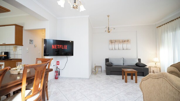 A modern living room with a flat-screen TV mounted on the wall, a sofa, a coffee table, and a dining area with chairs and a table. - Romance Dream Meteora 1 (Kalampaka, Greece)