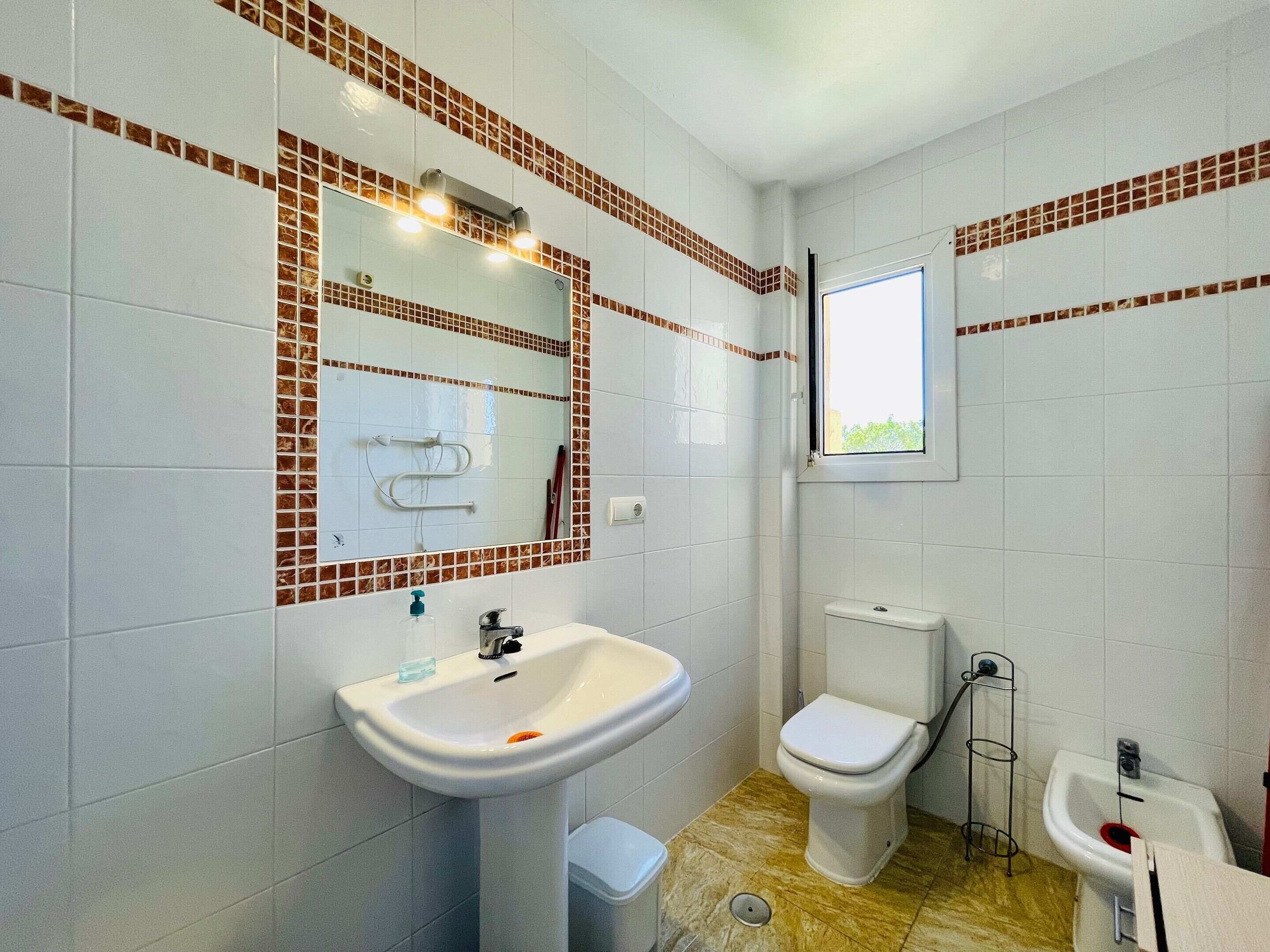 A bathroom with a sink, toilet, bidet, and a window.