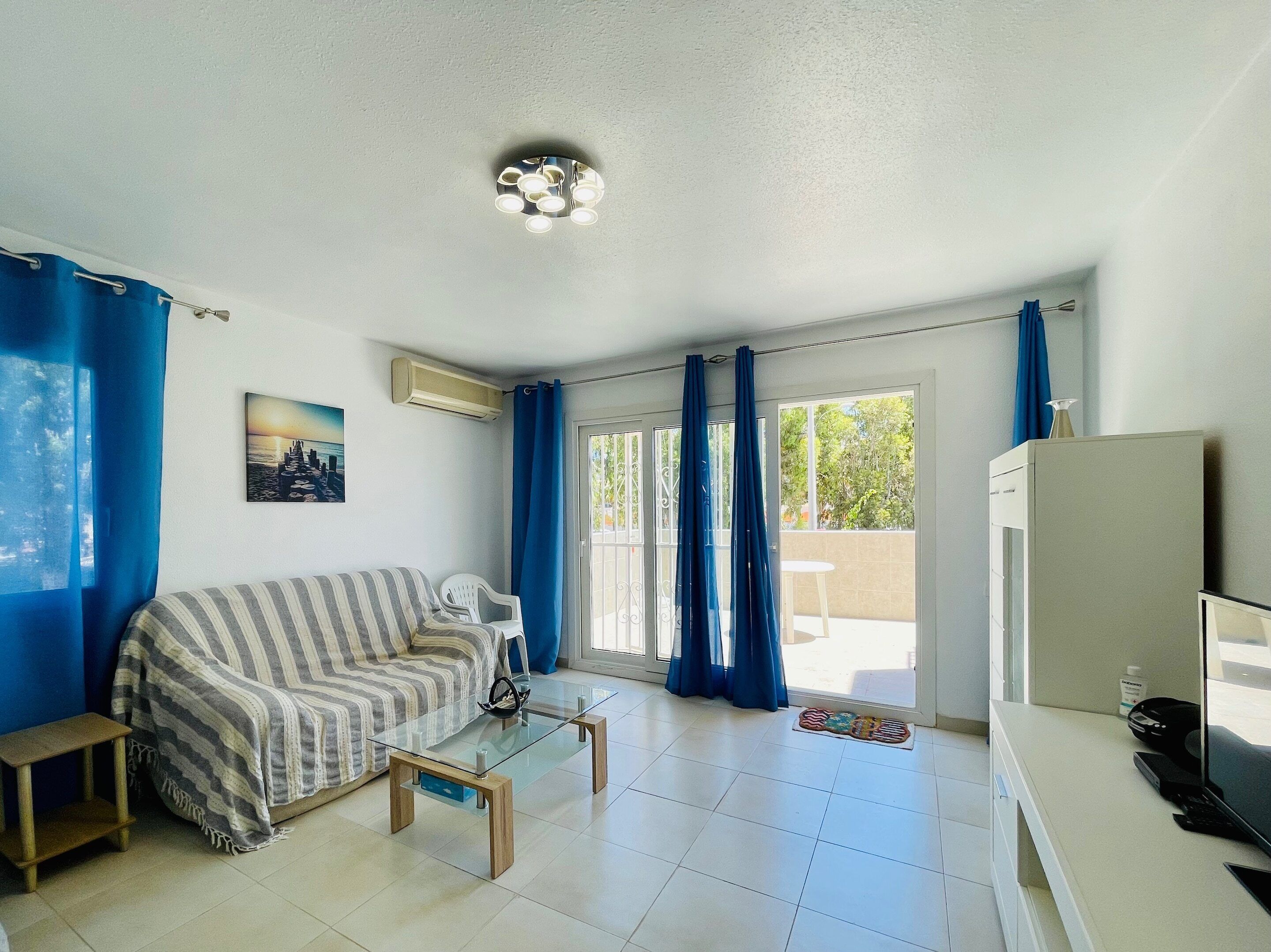 A compact living space with a sofa, a glass coffee table, a small side table, a refrigerator, and a door leading to an outdoor area.