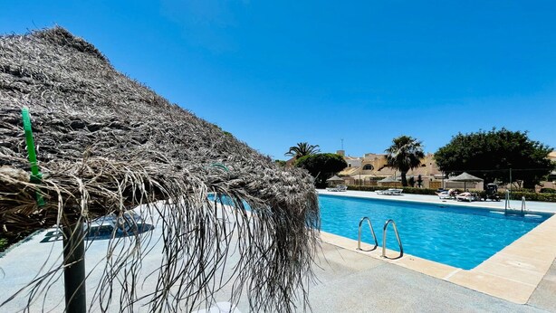 Una piscina con ombrellone di paglia, sedie a sdraio e cielo azzurro.