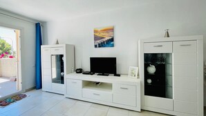 Un soggiorno moderno con una televisione a schermo piatto, un mobile TV bianco e un armadietto con bicchieri da vino.