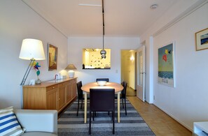 A dining area with a round table, chairs, a lamp, a cabinet, and a rug. - Chic Sea-view Apartment (De Haan)