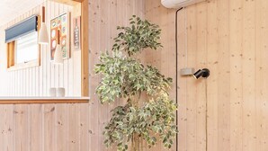 A room with wooden walls, a potted plant, a bed, and a window with blinds.