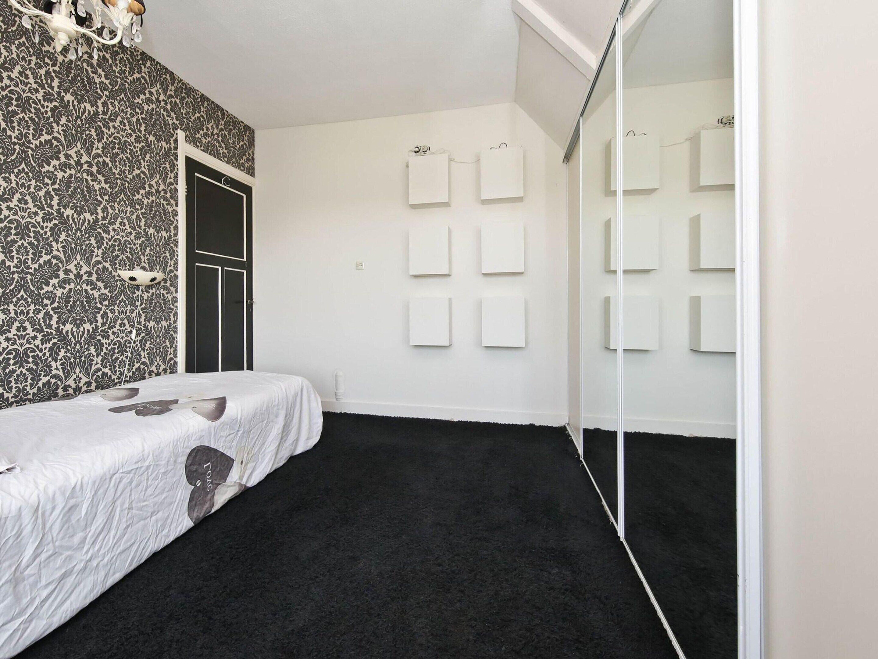 A bedroom with a bed, a black carpet, a patterned wallpaper, and a door.