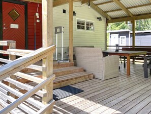 A covered outdoor area with a wooden deck, a glass table, wicker furniture, and a red door.