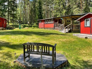 A wooden bench in a forested area with red cabins and a clear sky.