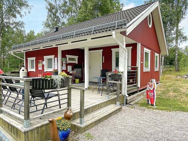 A red building with a wooden deck, outdoor seating, and a small garden area. - 8 Person Holiday Home in Rejmyre (Rejmyre)