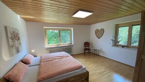 A bedroom with a wooden ceiling, a bed with pink bedding, a radiator, a window with a view of trees, and a heart-shaped decoration on the wall. - Appealing Apartment Near Lake (Argenbühl)