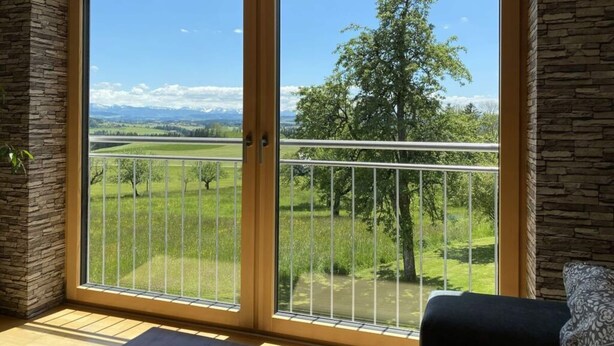 A room with a large sliding glass door leading to a balcony with a view of a green landscape and mountains. - Appealing Apartment Near Lake (Argenbühl)