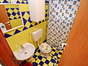 Une salle de bain avec un sol à carreaux jaunes et bleus, un lavabo blanc, des toilettes et un rideau de douche orné d’étoiles de mer et de motifs géométriques.