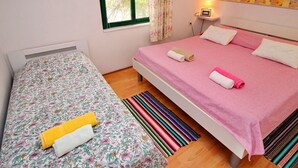 A bedroom with two beds, one with a floral bedspread and the other with a pink bedspread. There is a window with floral curtains, a bedside table with a lamp, and a striped rug on the floor. - Apartments Sunset - One Bedroom Apartment With Terrace and Sea View (Blato)