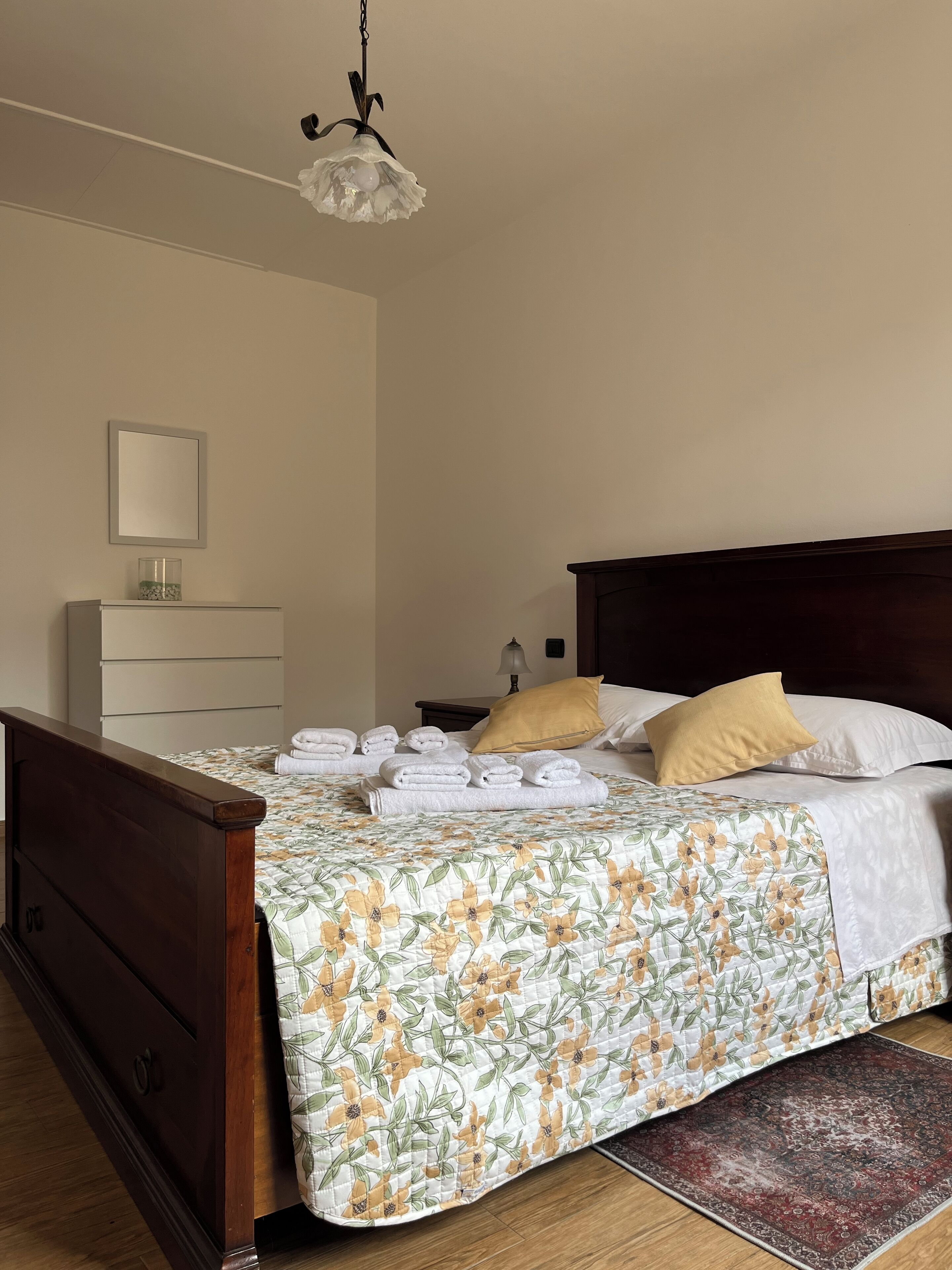 A neatly made bed with floral bedding, a wooden headboard, and a bedside table with a lamp.
