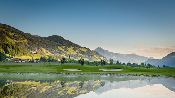 A serene golf course with a reflective pond, surrounded by lush green hills and mountains. - Chalet in Zillertal Near Ski Slopes (Aschau Im Zillertal)